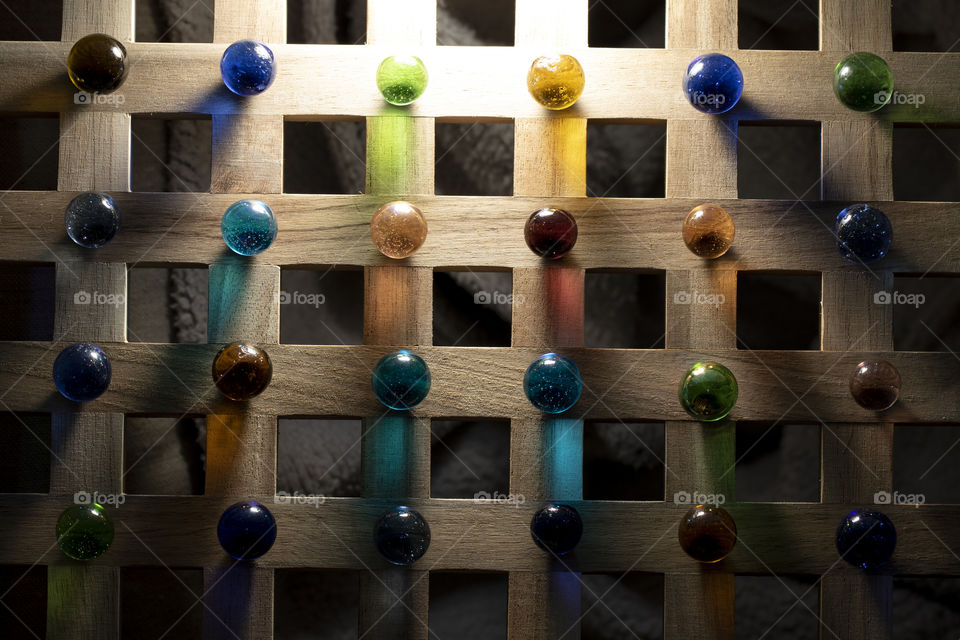 A colorful portrait of a wooden roster with colored marbles on it. the light shining through the marbles casts some colorful light on to the surface.