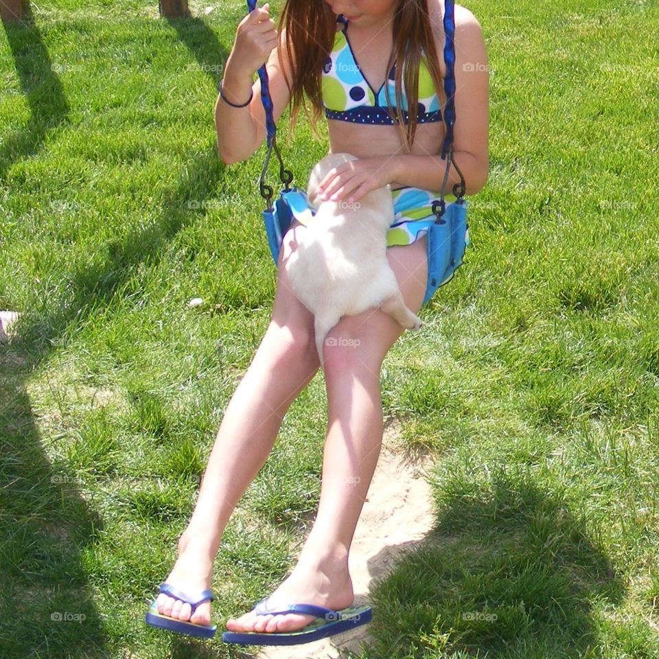 Young girl holding a yellow Labrador retriever puppy on her lap while sitting on a swing.