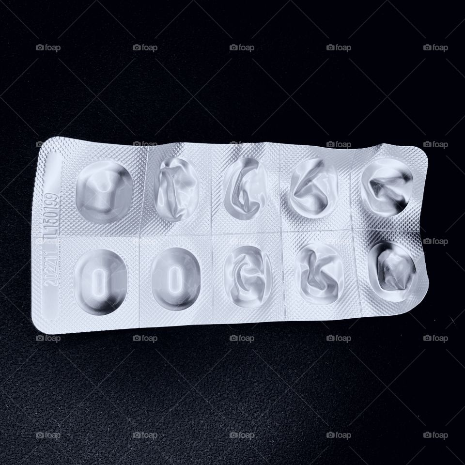 A pack of silver pills against a black background. Several of the pills have been taken out of the aluminum pack. 