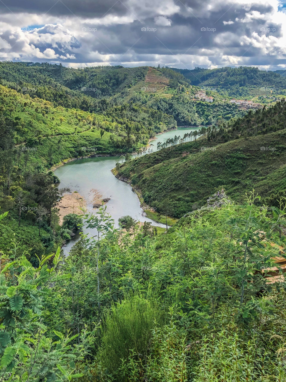 A green forested valley is lined by a flowing river, in Central Portugal 