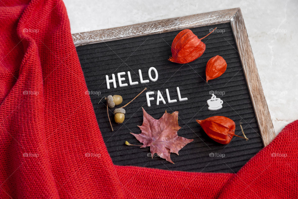Red warm sweater next to autumn leaves with words Hello fall 