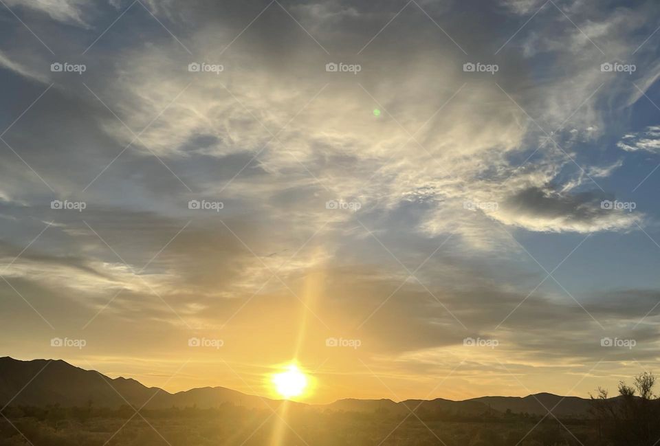 A sunset with clouds above and mountains below.