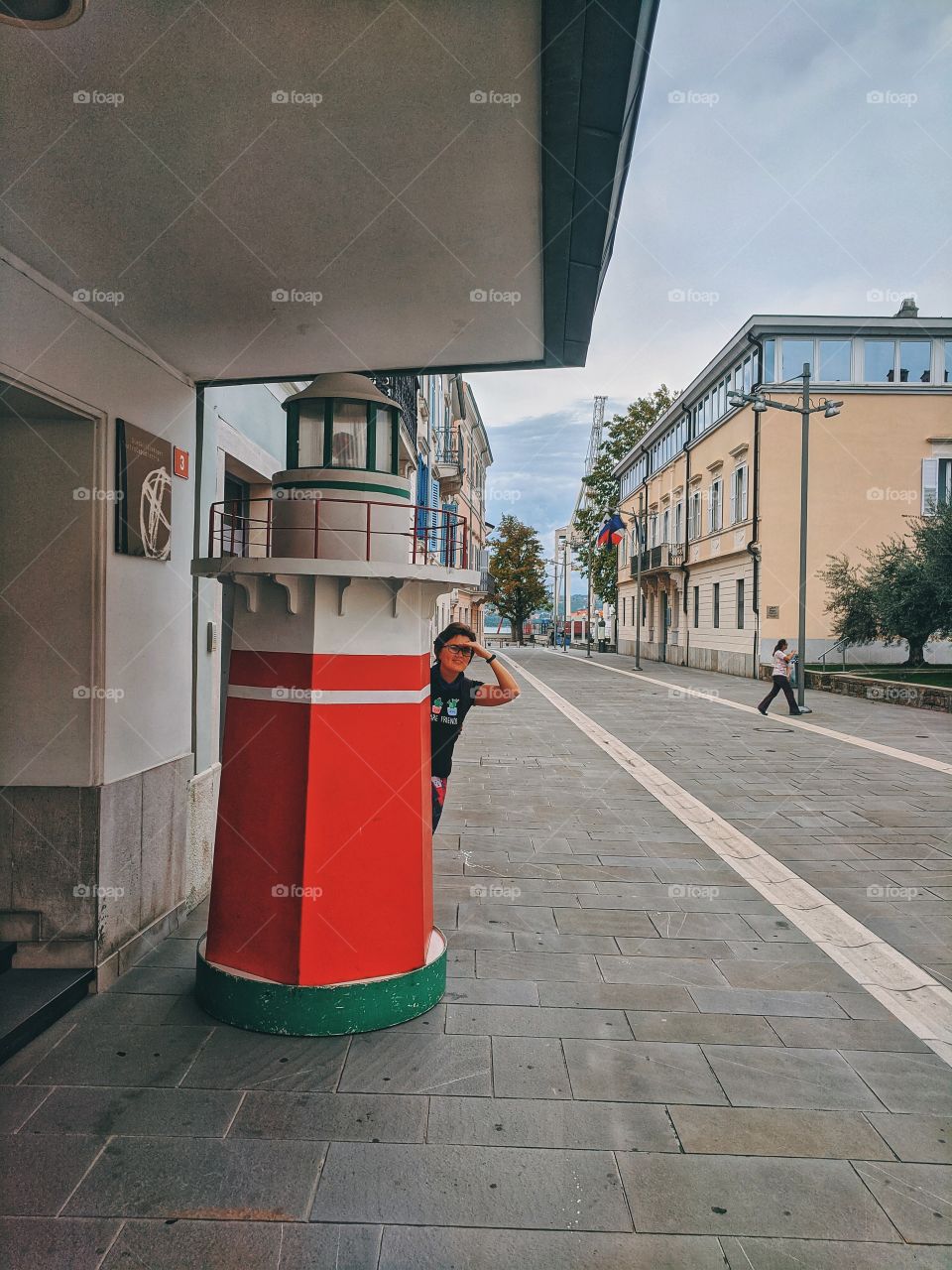 A funny girl looking out from behind a fake lighthouse.