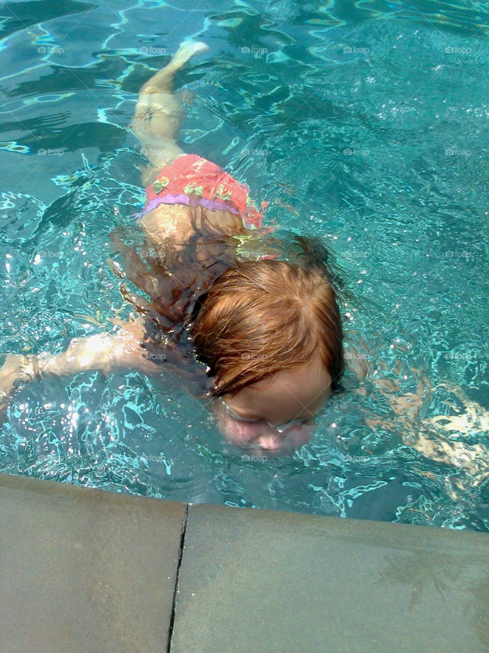 маленькая девочка с рыжими волосами ныряет в бассейне
