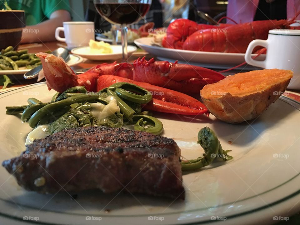 Surf and turf, fresh cooked lobster, steak, fresh wild steamed fiddleheads on plate on dinner table