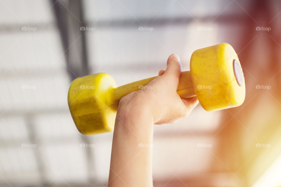 Kid working out with dumbbells in the sports hall of the club. Child hand holding yellow dumbbell
