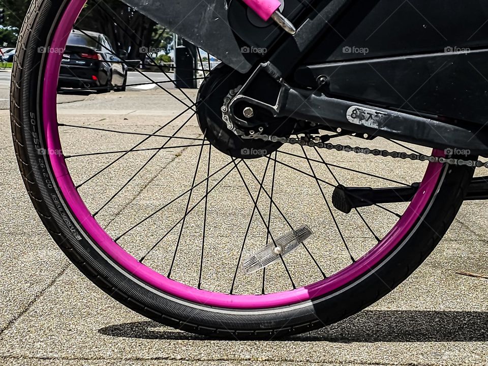 Sidewalk level view of a bicycle tire on the city sidewalk of San Francisco California with pink rims, abstract 