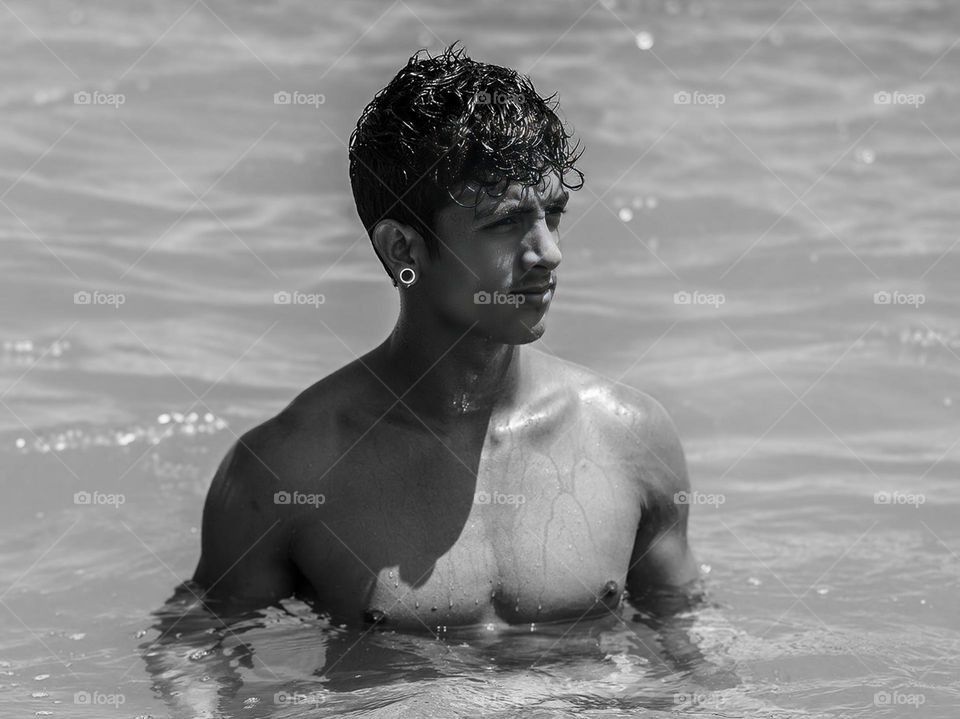 Portrait of a young man in the water, with his handsome face. This photo is black and white and looks artistic. The man is swimming or relaxing in the water