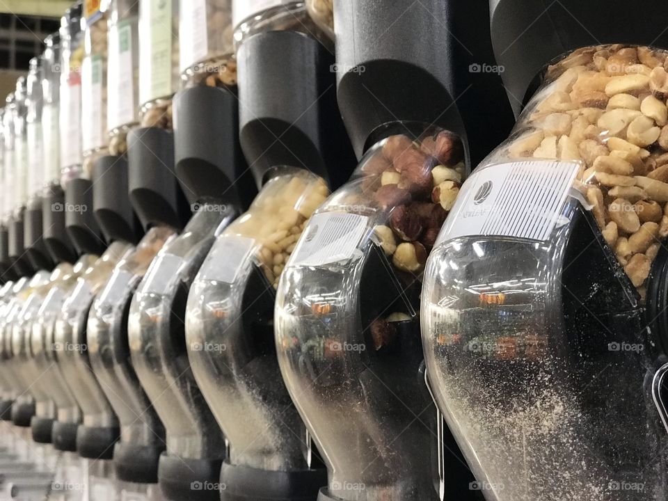 Rows of nuts and dried foods in their containers with self serve scoops in the bulk foods section of the grocery store. 