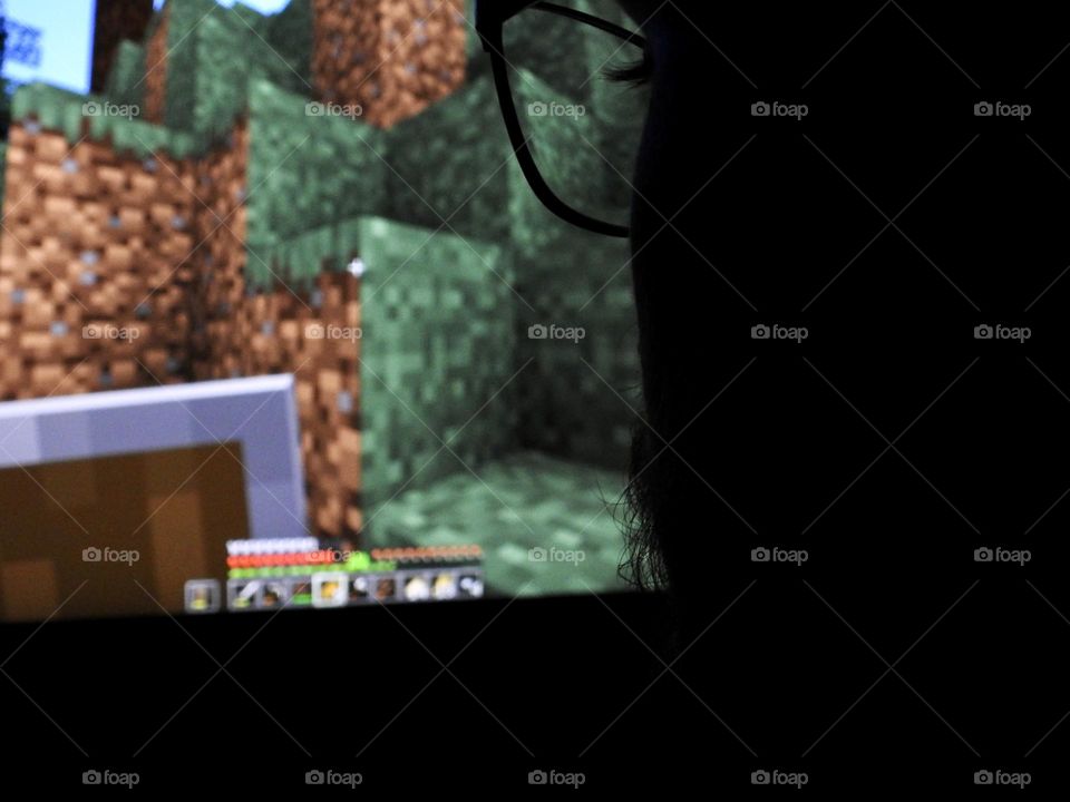 Teenager boy playing Minecraft on the gaming computer seen from his glasses close-up in a dark room.