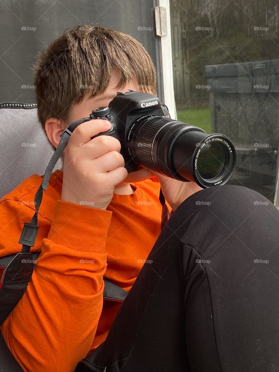 Person in orange shirt looking through camera viewfinder.