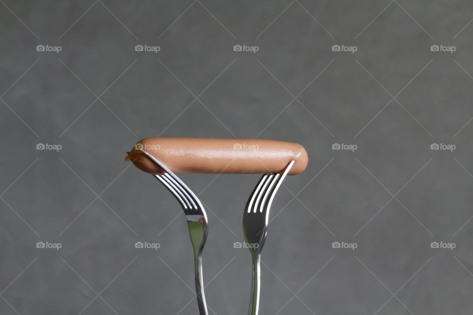 One fork is pierced with one hot dog during times of famine and lack of food with sunlight and shadows.