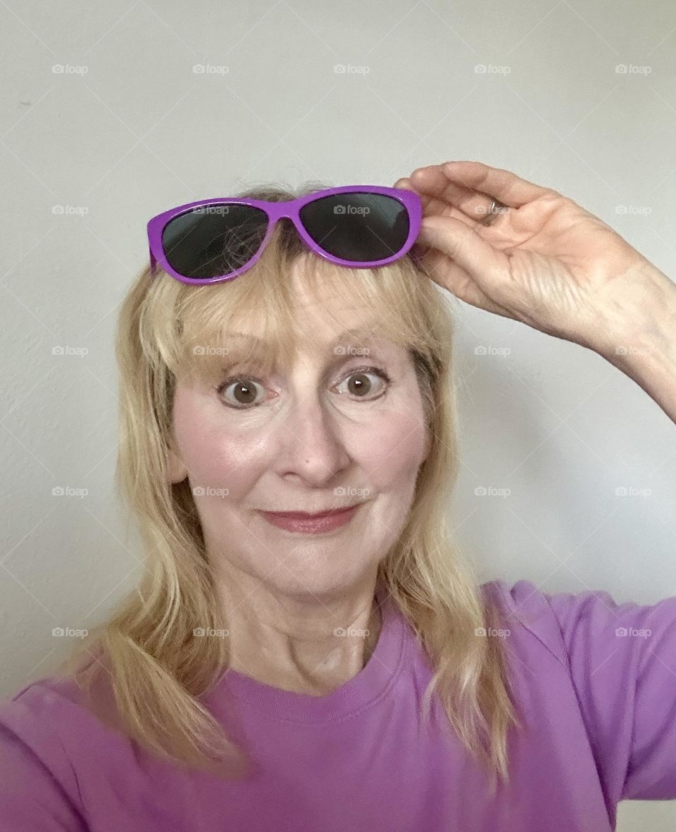 Woman with surprised expression with purple sunglasses on her head