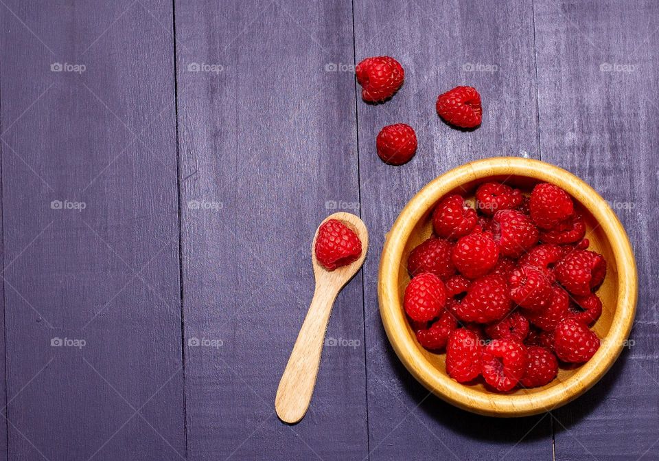 Fresh; organic raspberries on a wooden bowl with a wooden spoon on a black wood background 