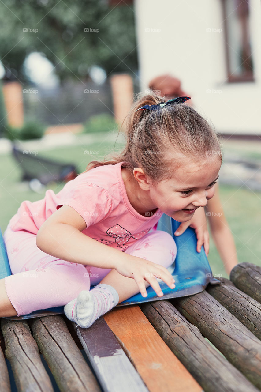 Little adorable girl playing in a home playground in a backyard. Happy smiling kid having fun on a slide on summer day. Real people, authentic situations