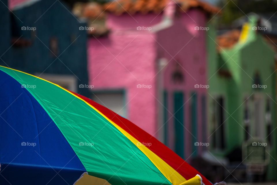 Rainbow colored beach umbrella on a warm summer day with the colorful buildings of the Venetian in Capitola by the Sea in the background 