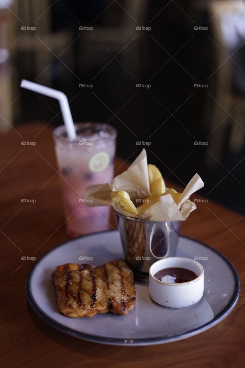 Delicious grilled chicken BBQ and french fries served on plate and refreshing frozen berry juice at a restaurant