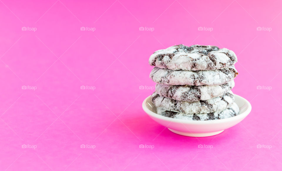 Handmade chocolate cookies with sugar powder on white plate at pink background.
