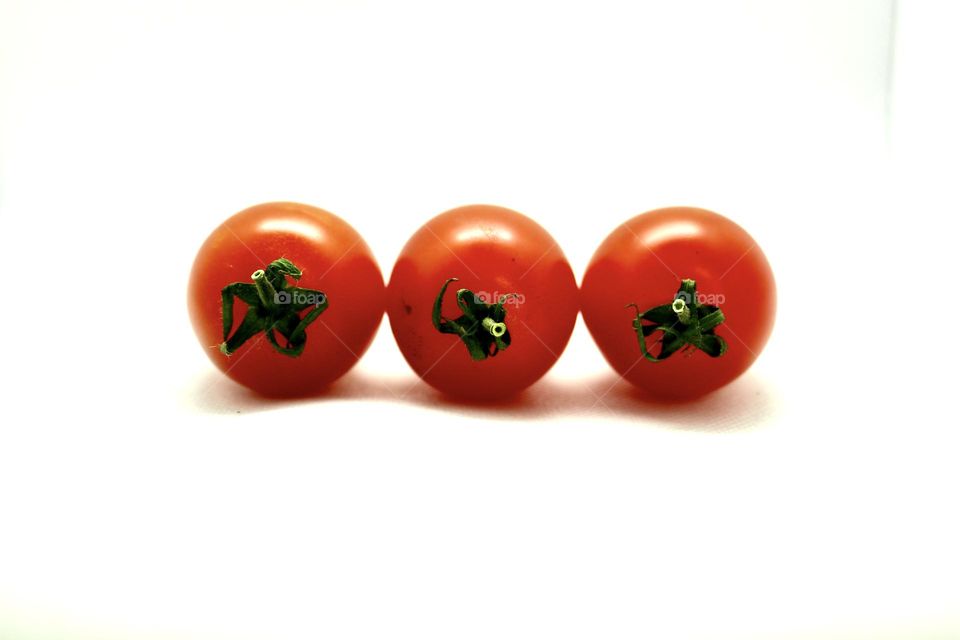 A trio row of ripe organic cherry tomatoes stems facing camera isolated on white background backdrop, room for text, concept repetition, teamwork, food and nutrition