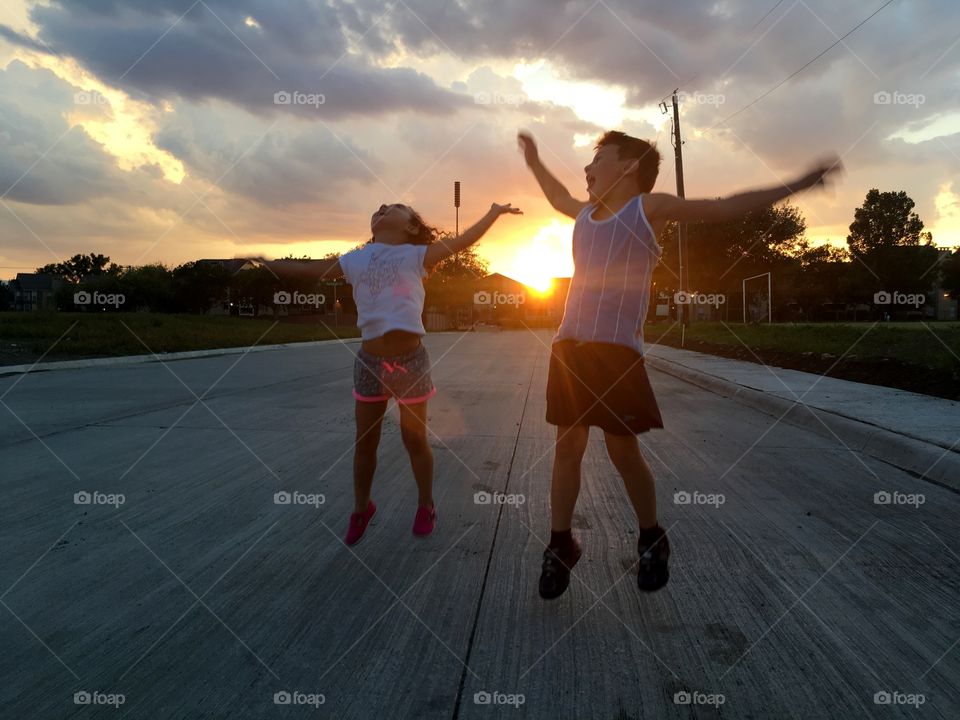 two children, one girl and one boy jumping and having fun during a sunset