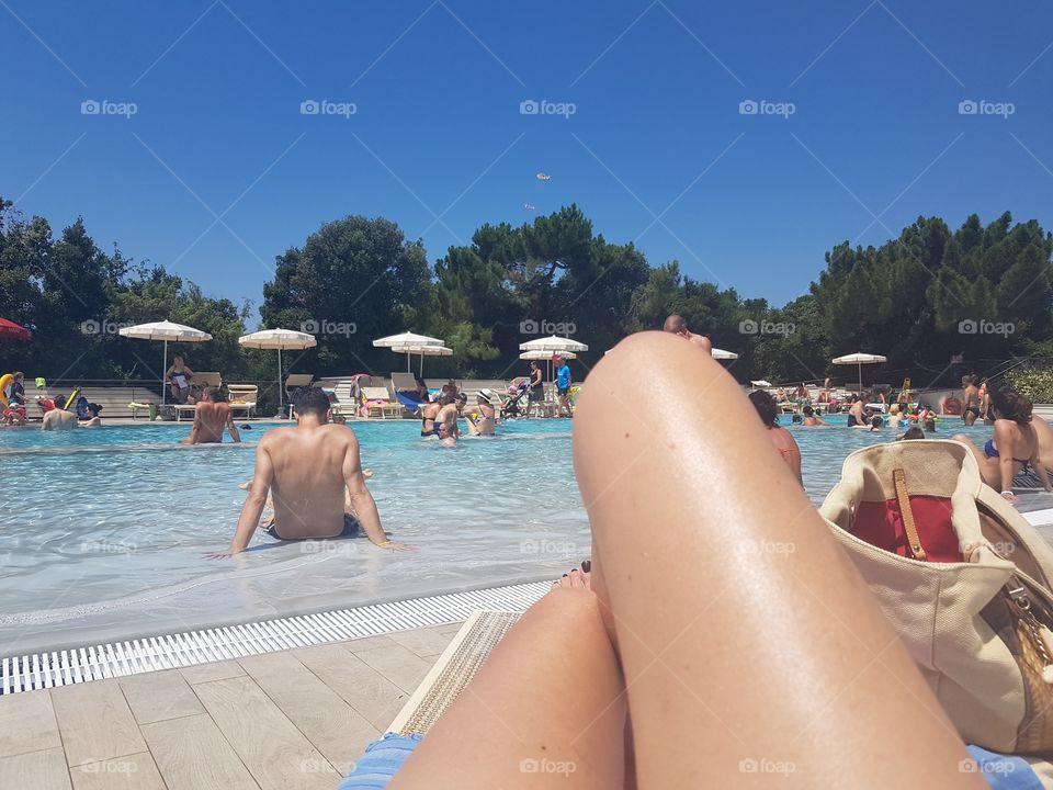 Swimming pool with woman legs close-up and blue sky in Tuscany, Italy