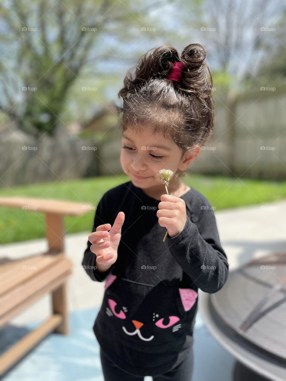 Little girl rubs dandelion on cheek, playing with weeds, dandelions everywhere, picking dandelions with toddlers, fun outside in the spring 