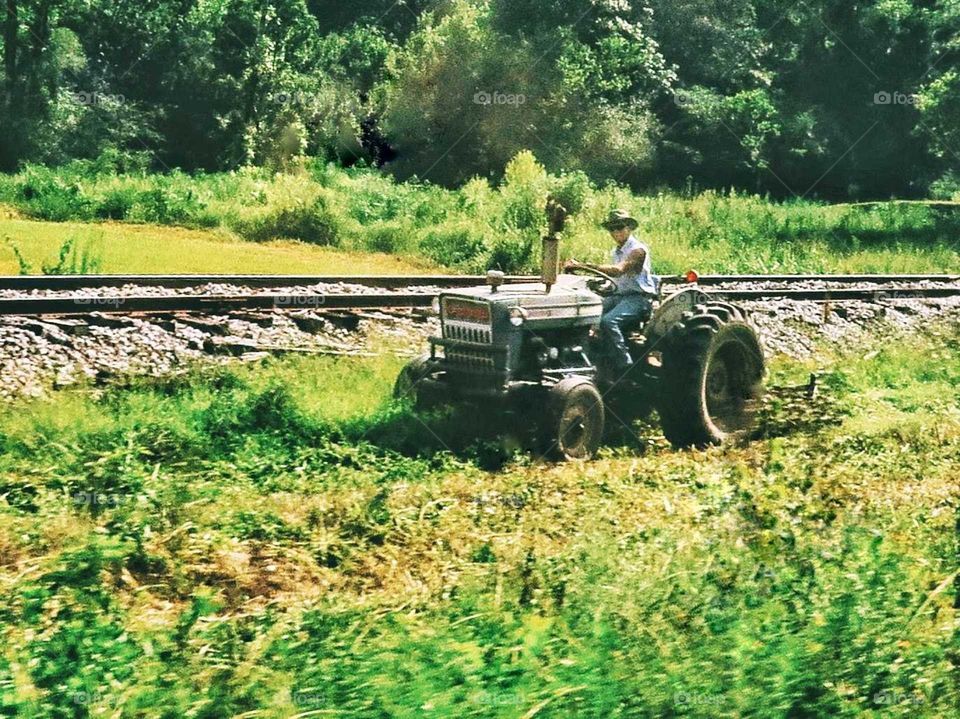 A farmer bush hogging a patch of land running parallel with train tracks