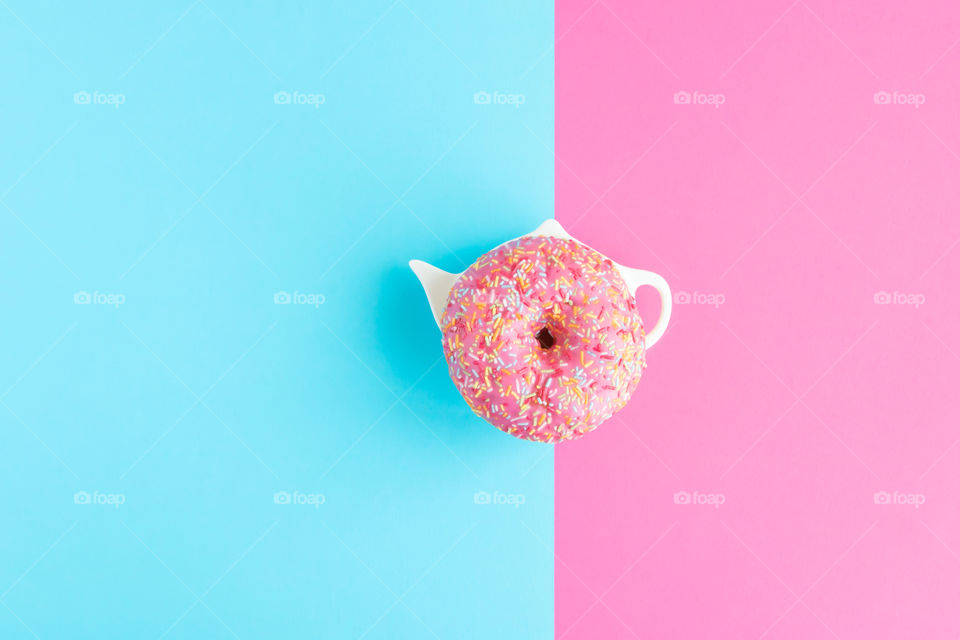 Donut covered with pink icing and topping on pink and blue pastel colours background.