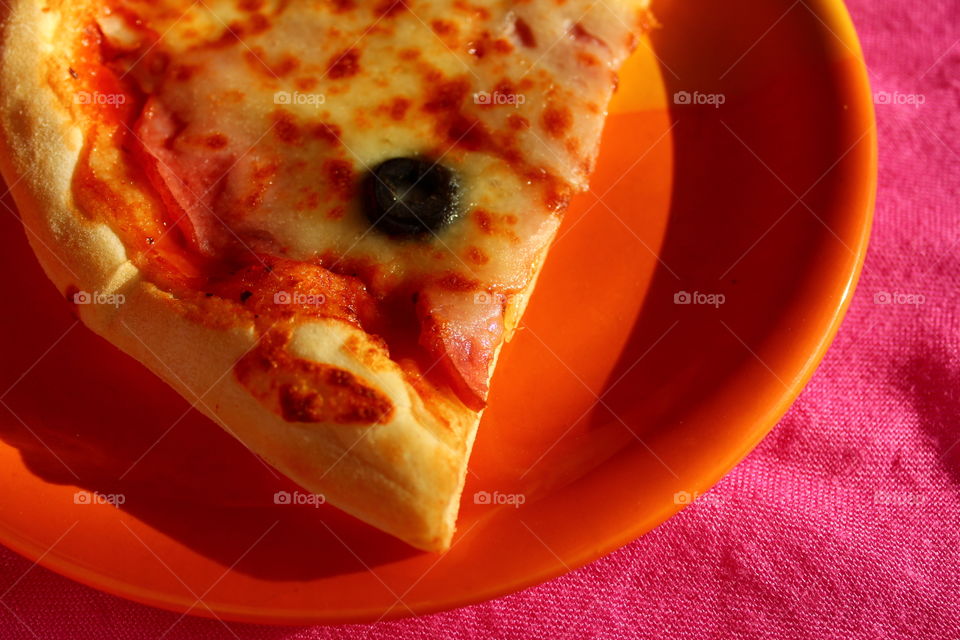 Slice of pizza in a orange plate on a pink background