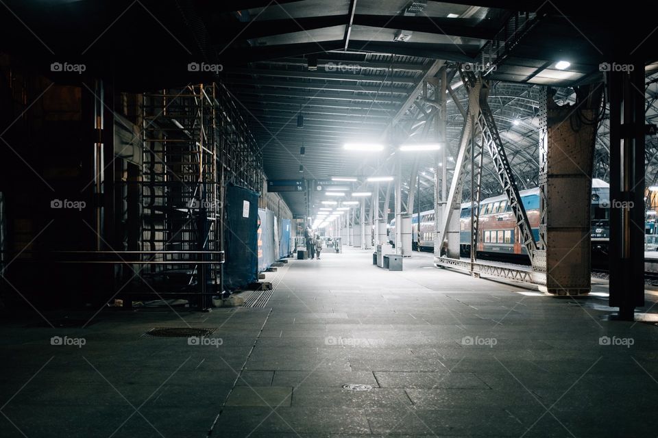 Quiet Train Station with fluorescent lights. Two people stand in the distance and the train waiting for passengers to the left.