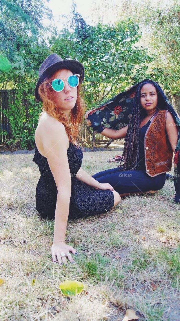 Two female friends sitting on grassy landscape
