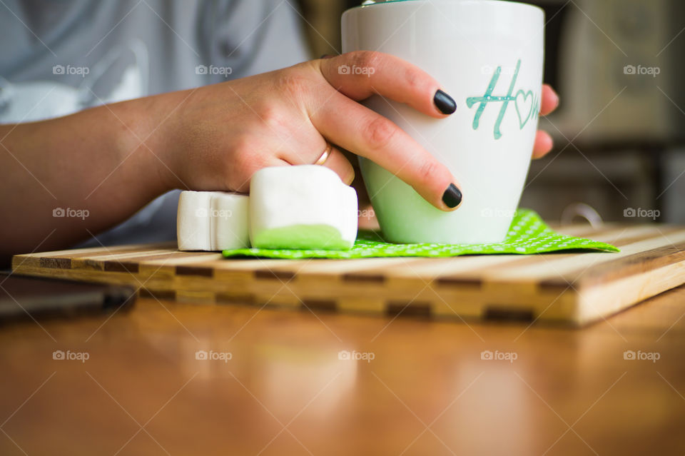 Hands of a girl close-up who drinks coffee in a cafe from a cup with the inscription at home