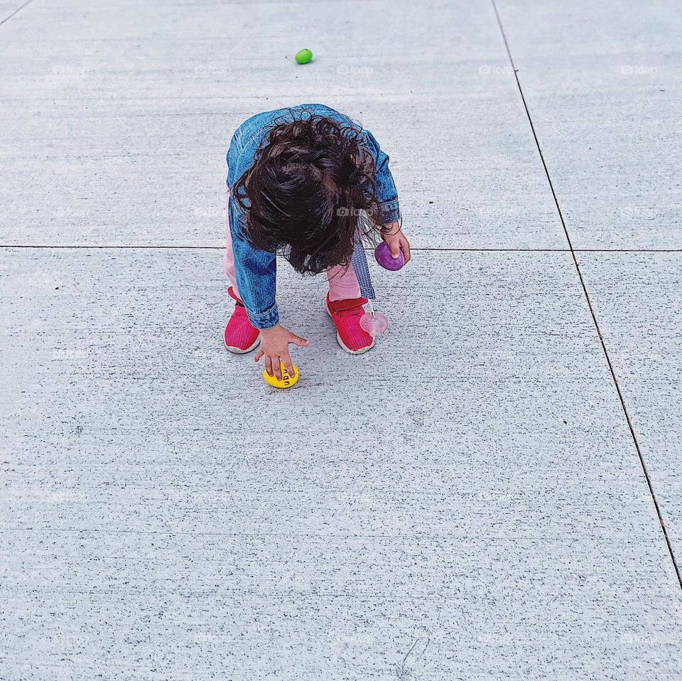 Toddler girl picking up plastic Easter eggs, toddler at an Easter Egg Hunt, Easter Traditions, toddler picks up Easter Eggs, toddler on the hunt