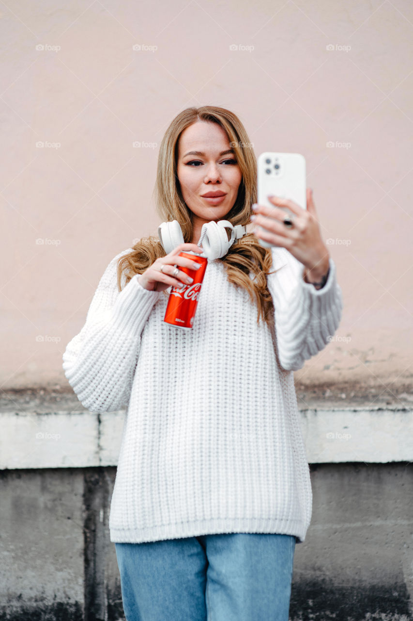 A woman in white sweater making selfie with Coca-Cola can