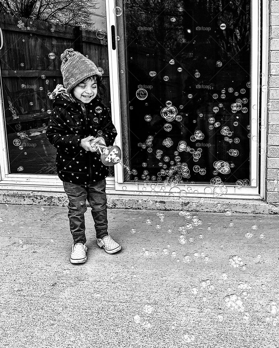 Child playing with bubble maker outside, bubbles in the winter time, toddler girl loves blowing bubbles outside on patio, toddler girl having fun with bubbles, circular bubbles fill the frame, monochrome bubble joy 