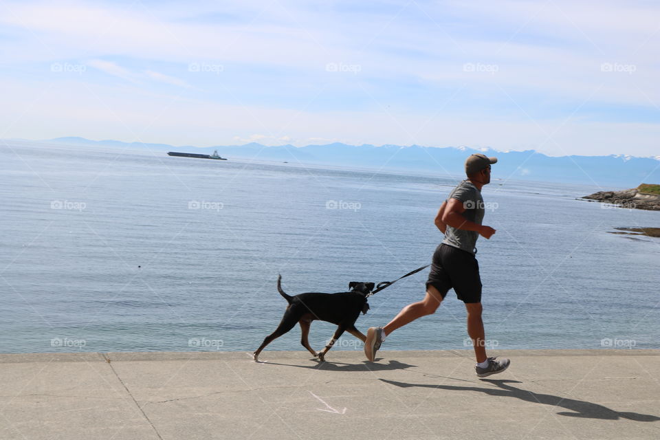 A man and his dog running by the ocean on a warm and calm sunny day