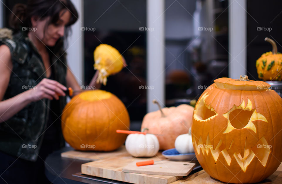 Woman carving pumpkins at home in kitchen selective focus on jack o’lantern 