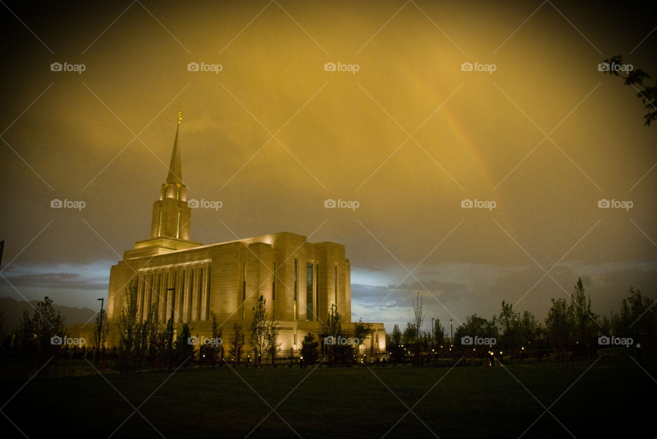 The LDS Oquirrh Mountain Temple at sundown with a passing storm and a hint of a rainbow arching close by