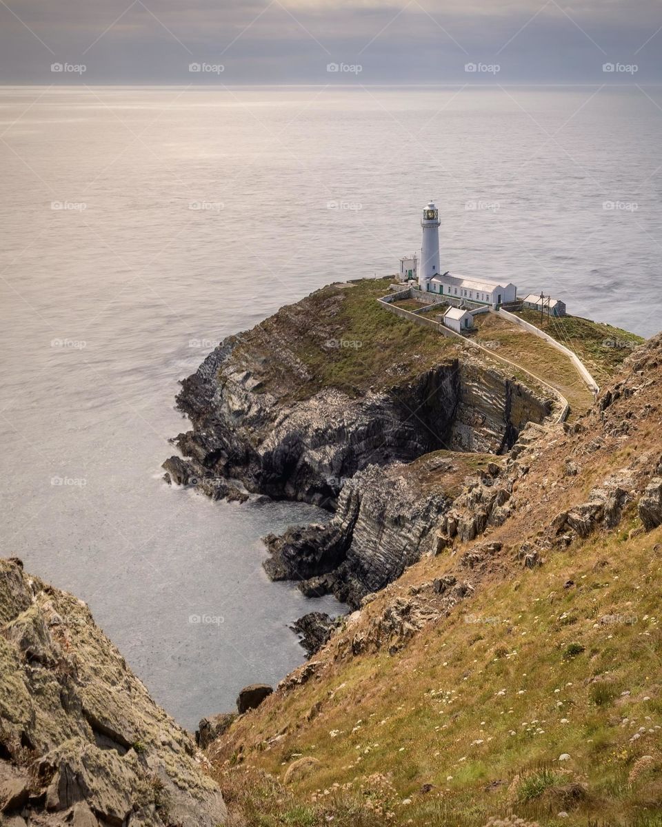 Epic seascape with a tall lighthouse sitting at the edge of a dramatic rugged coastal cliff at sunset 