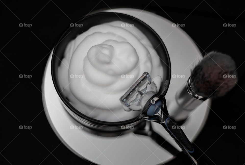 Shaving razor on porcelain more with shaving foam and organic shaving brush standing on a round small mirror on a black background, flat lay close-up. Concept barbershop men, shaving men, beard care.