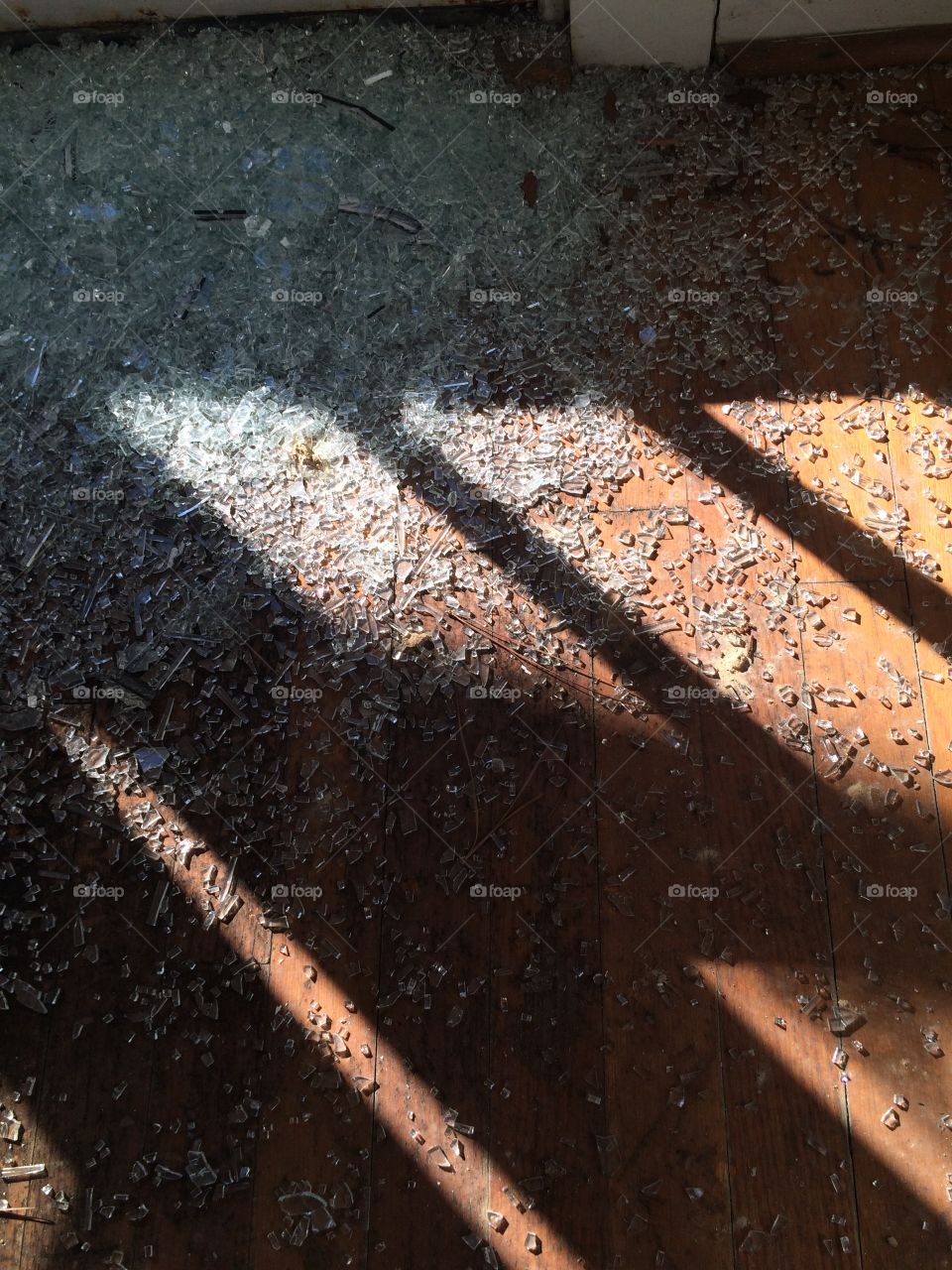 Shards of sparkling glass strewn across an old wooden floor. The light from the window streaming in geometric patterns. 