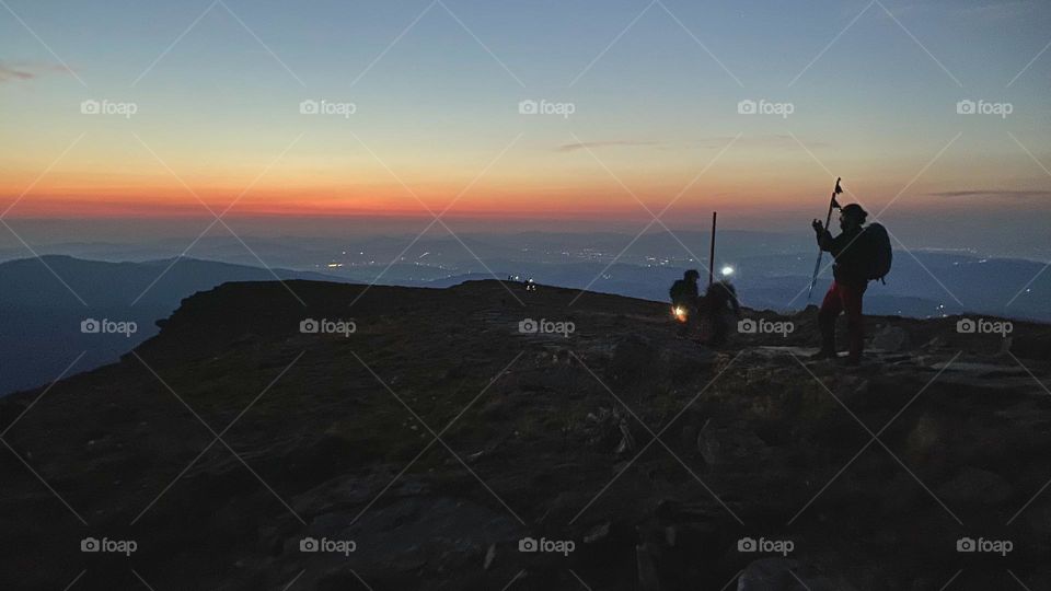 People hiking at night to see sunrise. Mountains at sunrise. Man standing on peak. Natural mountain landscape with illuminated misty peaks, foggy slopes and valleys, blue sky with orange yellow sunlight. Amazing scene from Beskid Zywiecki in Poland