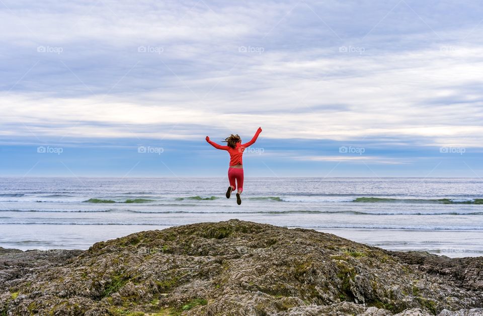 Girl jumping off rock outcropping at the Pacific Ocean bear Tofino, Canada 