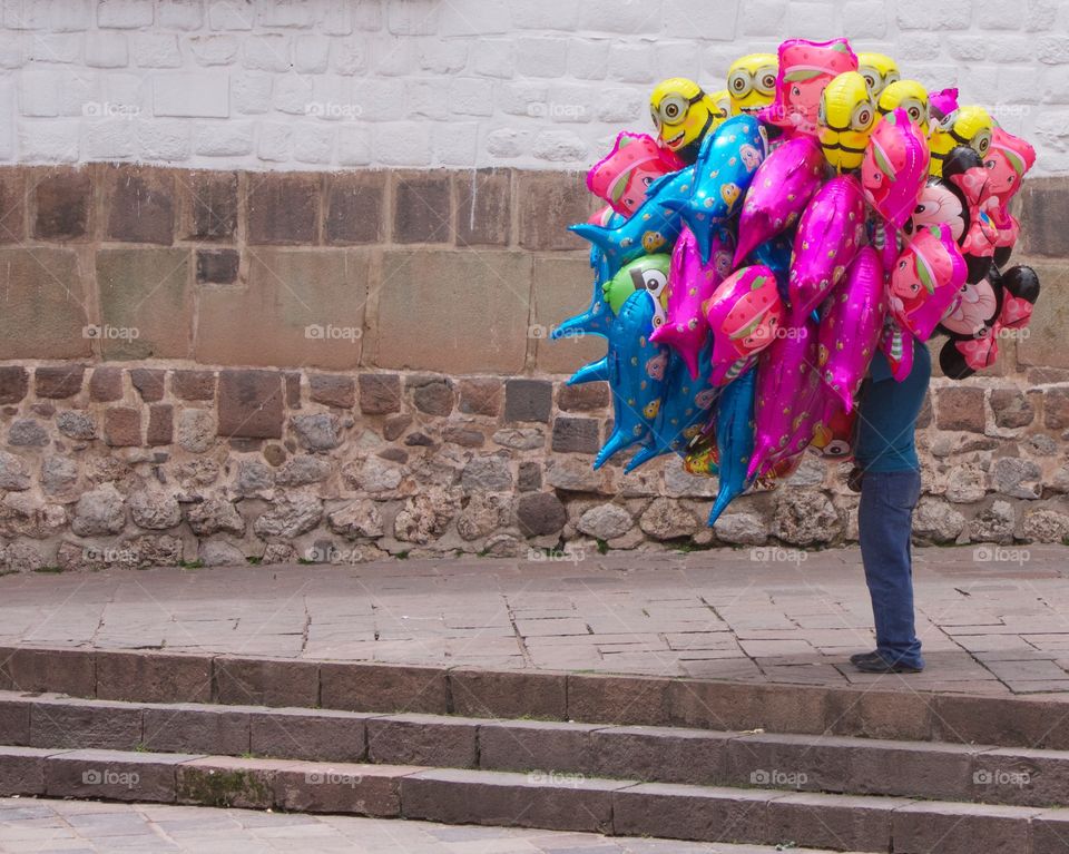 A person selling colorful helium balloons on the street in Cisco, Peru with the entire inventory of balloons covering the person's face and feet.