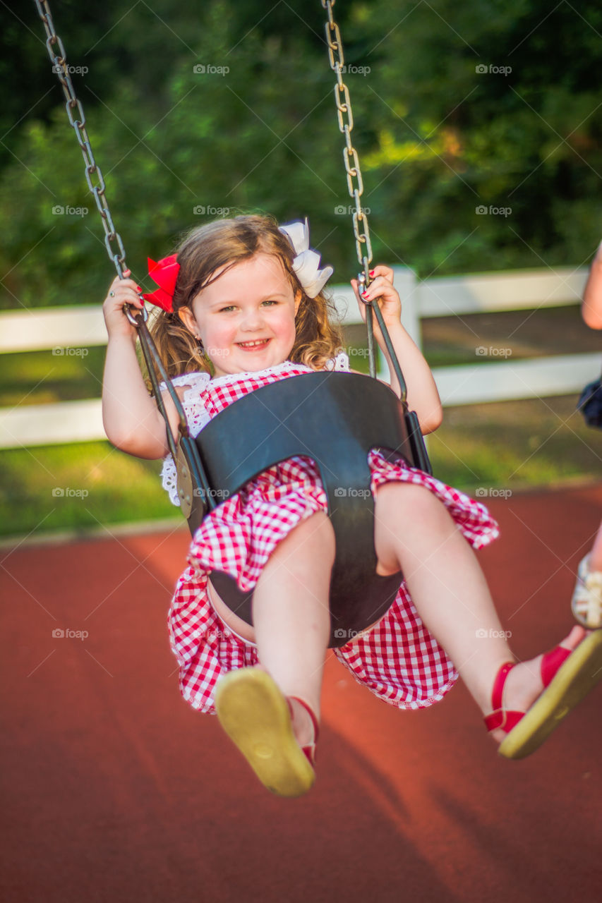 Young Girl on Swing at a Playground in Red Gingham Dress