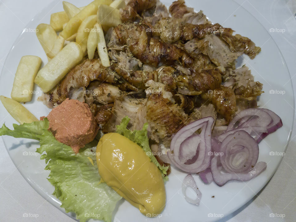A portion of Greek chopped gyros with pork meat, fried potatoes, onions, mustard and ketchup, served on a white plate.