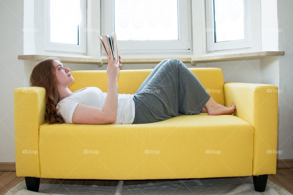 Woman lying on sofa and reading book