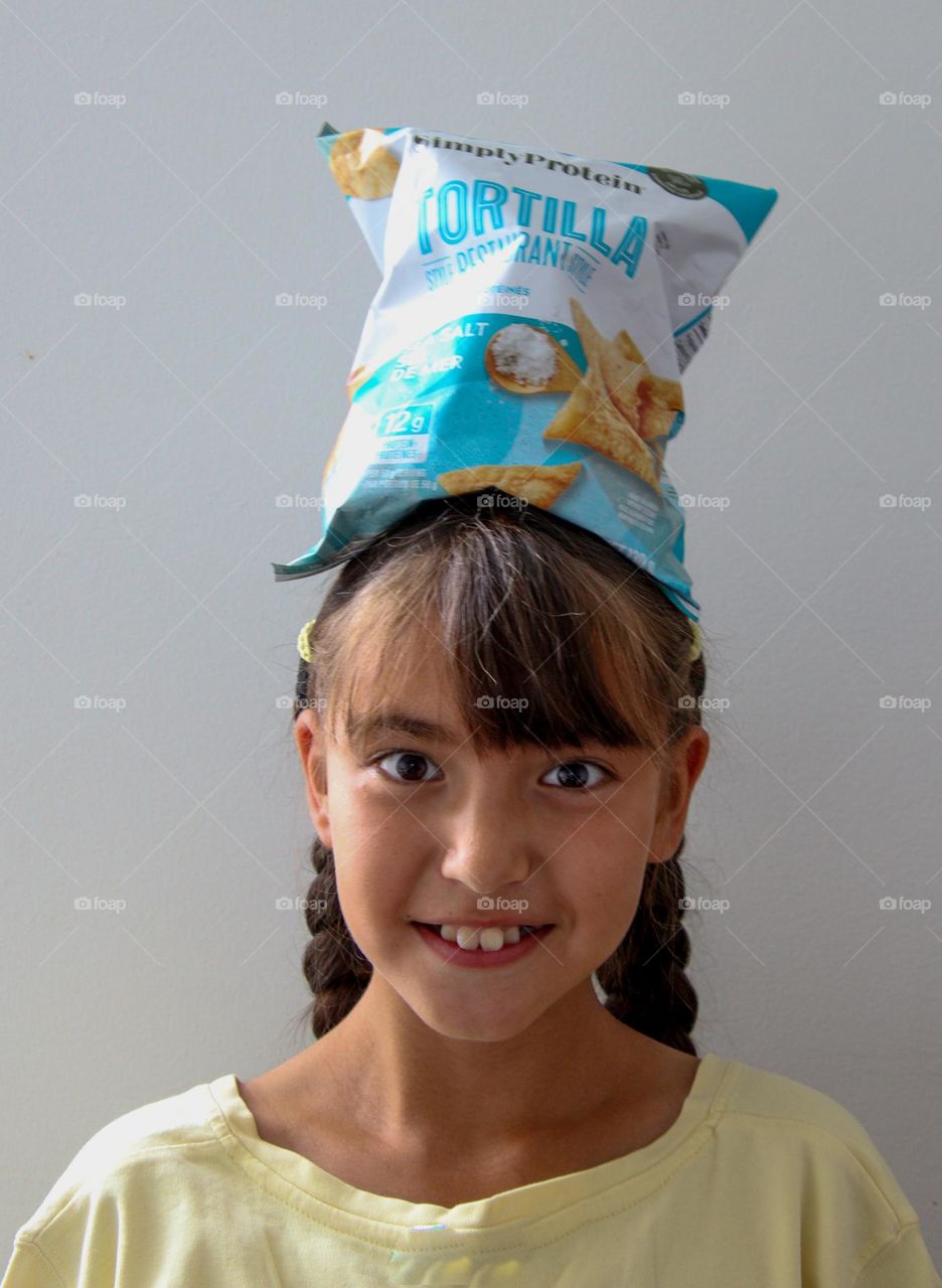 Cute happy girl balancing bag of chips on her head