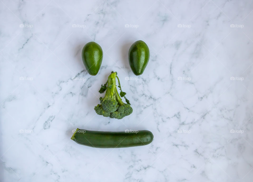 Top view to green fresh vegetables in shape of smiling face on marble background.