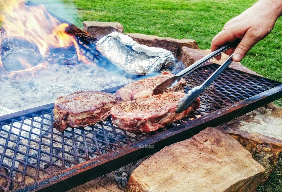 Man's hand turning steaks over an open fire pit summer memories